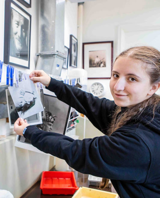 Young student hanging black and white prints to dry in a traditional darkroom setup. Young student hanging black and white prints to dry in a traditional darkroom setup.